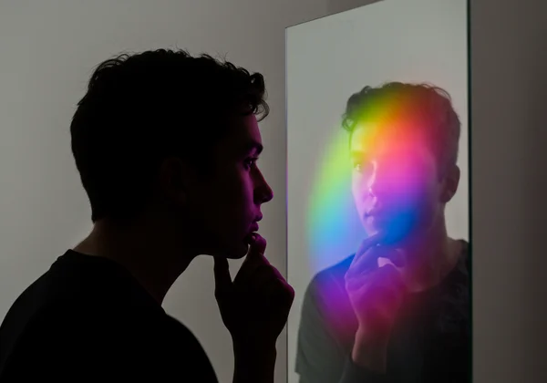 Person in thoughtful pose looking at colorful reflection.